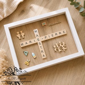 Könnte beinhalten: Ein weiß gerahmtes Kunstwerk mit dem Namen "MARIE-PIERRE" in Scrabble-Buchstaben. Der Rahmen enthält Holzausschnitte von Kindern, Schulmaterialien und das Wort "Maternelle".