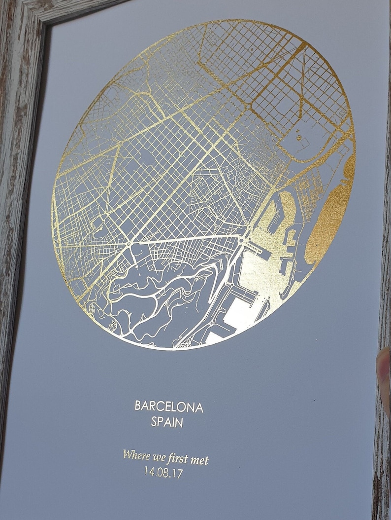Op de afbeelding: Een gouden folie-afdruk van een kaart van Barcelona, Spanje. De afdruk is ingelijst en heeft de tekst "Barcelona Spain Where we first met 14.08.17" onder de kaart gedrukt.