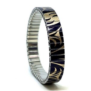 Puede incluir: Un brazalete extensible de plata con un diseño estampado en negro y dorado. El patrón presenta un diseño repetitivo de hojas y espirales estilizadas.