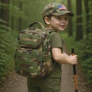May include: A camouflage backpack and cap with an American flag patch. The backpack has multiple compartments and straps. The cap is worn by a person in a green shirt and pants, holding a walking stick, walking on a path in a forest.