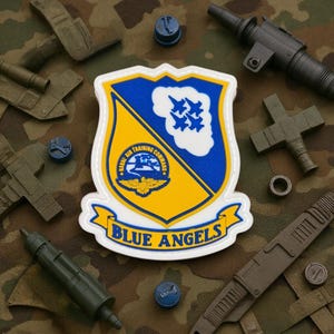 May include: A white-bordered patch with a blue and yellow shield design, featuring the text "BLUE ANGELS" on a banner. The shield includes a cloud with four blue jets and the words "NAVAL AIR TRAINING COMMAND". Surrounding the patch are miniature military-themed accessories.