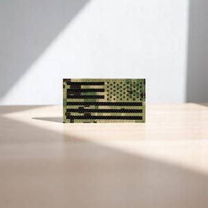 May include: A green, brown, and black camouflage fabric American flag patch with black stars and stripes.