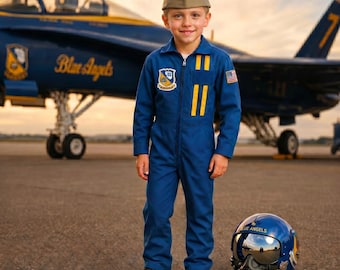 May include: A young person in a blue jumpsuit and a khaki cap stands in front of a Blue Angels jet. The jumpsuit has yellow stripes and patches. A blue helmet with the words "Blue Angels" is on the ground.