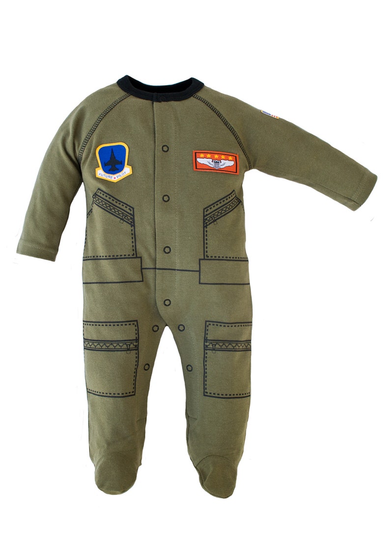Puede incluir: Mono de beb&eacute; verde oliva con cuello negro y mangas largas. El mono presenta un tema de piloto con parches, incluyendo un avi&oacute;n azul y el texto "FUTURE PILOT". Tiene una botonadura y pies.