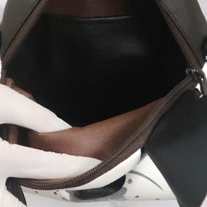 K&ouml;nnte beinhalten: Eine braune und wei&szlig;e Rei&szlig;verschlusstasche mit braunem Futter. Die Tasche ist offen und das Futter ist sichtbar.