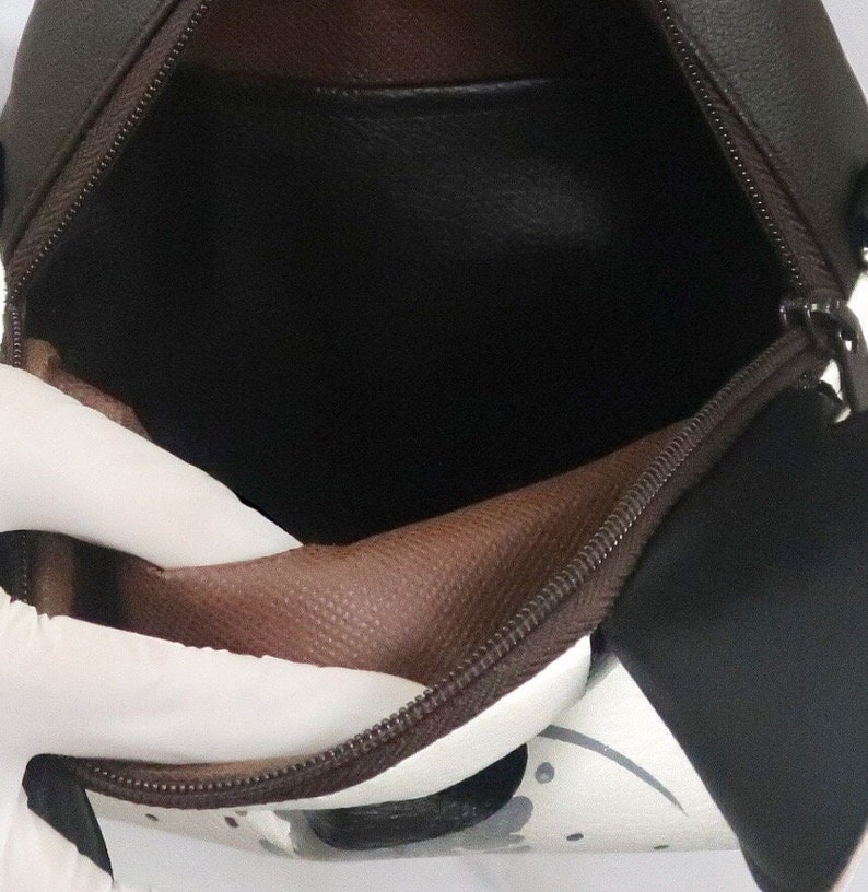 K&ouml;nnte beinhalten: Eine braune und wei&szlig;e Rei&szlig;verschlusstasche mit braunem Futter. Die Tasche ist offen und das Futter ist sichtbar.