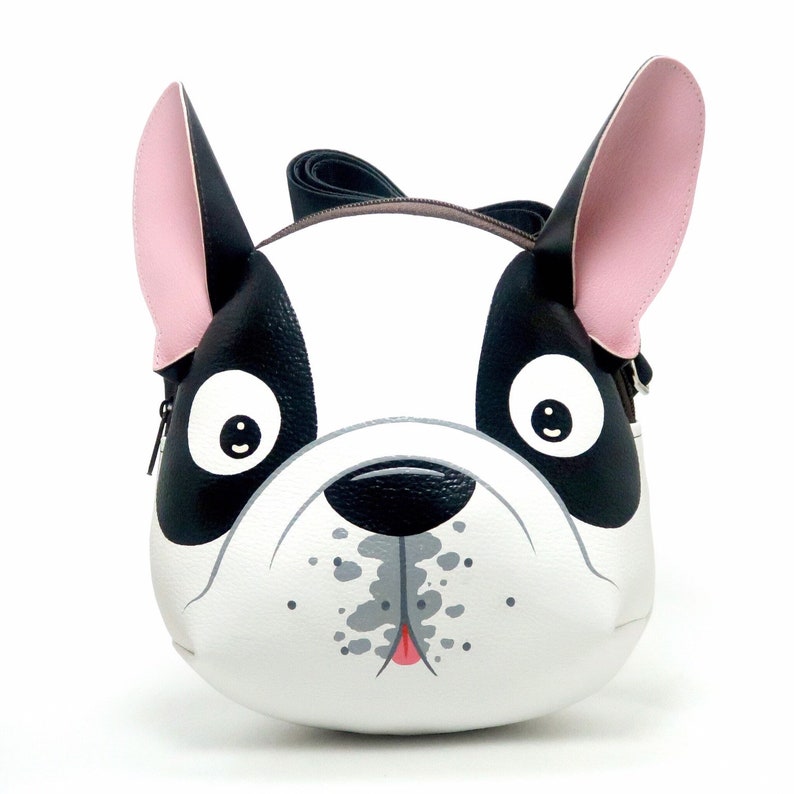 K&ouml;nnte beinhalten: Ein schwarzer und wei&szlig;er Rucksack in Form einer Franz&ouml;sischen Bulldogge mit rosa Ohren. Der Rucksack hat einen Rei&szlig;verschluss und einen Riemen.