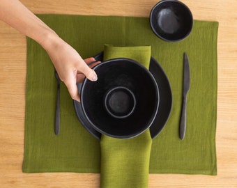 Könnte beinhalten: Eine schwarze Schüssel und ein Teller auf einem grünen Platzdeckchen mit einem schwarzen Messer und einer Gabel. Das Platzdeckchen liegt auf einem Holztisch.