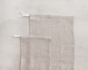 May include: Two beige linen reusable shopping bags with white drawstrings. The bags are stacked on top of each other.