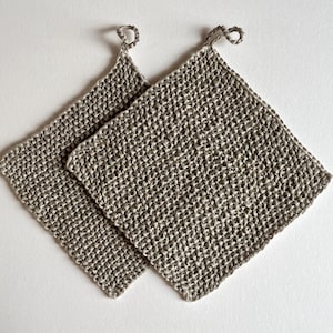 May include: Two square, light brown, crocheted potholders with a textured, grid-like stitch pattern. Each potholder features a small, matching crocheted loop at one corner for hanging, showcasing a consistent, neutral-toned yarn construction.