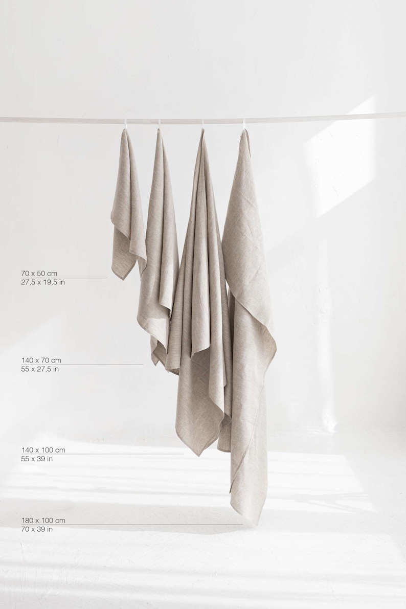 May include: Four linen towels of different sizes hanging on a clothesline. The towels are all a light beige color. The measurements of each towel are listed below the towels in inches and centimeters.