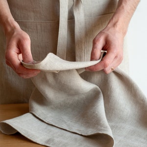May include: A person is holding a beige linen tea towel, showing the texture and weave of the fabric.