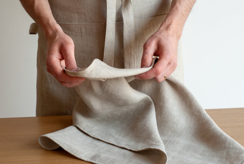 May include: A person is holding a beige linen tea towel, showing the texture and weave of the fabric.