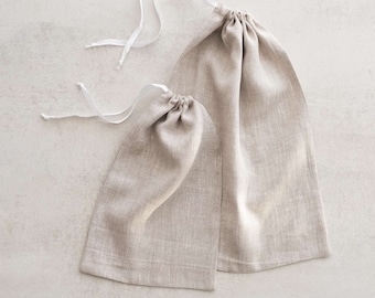 May include: Two beige linen drawstring bags with white drawstrings. The bags are made of natural fabric and are perfect for storing small items.