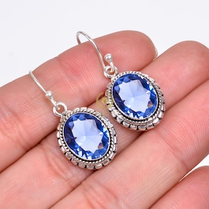 Peut inclure: Une paire de boucles d'oreilles pendantes en argent avec des pierres précieuses ovales bleues. Les pierres précieuses sont serties dans une bélière en argent avec une bordure décorative.