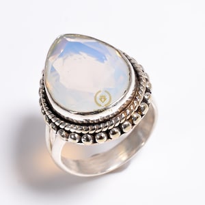 Könnte beinhalten: Ein silberner Ring mit einem birnenförmigen weißen Opal-Edelstein, der in einer geperlten und gedrehten Silberbandfassung sitzt.