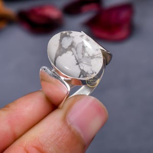 May include: A silver ring featuring a white and grey oval gemstone. The ring has a distinctive design with a curved band.