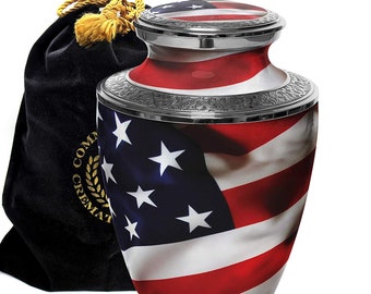 May include: A silver urn with an American flag design. The urn has a silver lid and is decorated with a silver trim. The urn is sitting on a white surface. It comes with a black velvet bag.