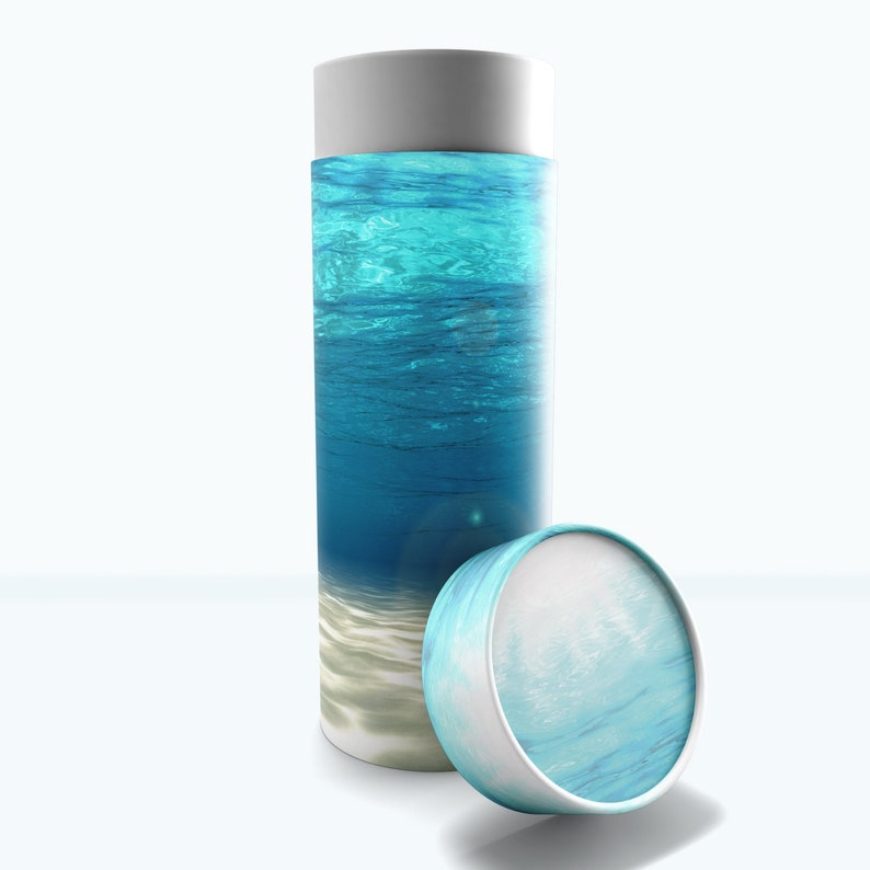 May include: A white cylindrical container with a blue and white design. The container is open and the lid is lying next to it. The design on the container features a blue ocean with white sand at the bottom.