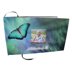 May include: A teal blue butterfly with black markings on a blue and green background with a photo of a woman in a window. The text "A Celebration of Life" is printed below the photo.