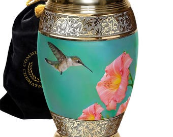 May include: A gold urn with an engraved design and a teal background featuring a hummingbird and pink flowers. The urn comes with a black velvet bag.