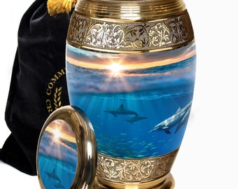 May include: Brass cremation urn with a sunset and dolphin image. The urn has an engraved border and comes with a black velvet bag.