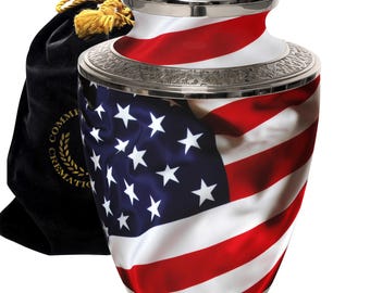 May include: Silver cremation urn with an American flag design. The urn has a lid and is decorated with a silver trim. It comes with a black velvet bag.