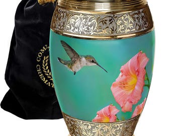 May include: Gold urn with a teal background and a hummingbird flying over pink flowers. The urn has an ornate gold design around the top and bottom.