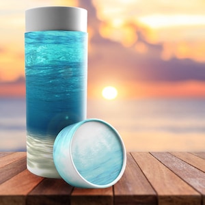 May include: A white cardboard tube with a blue and white ocean-themed design. The tube is lying on a wooden surface.