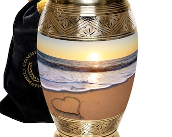May include: Gold cremation urn with a beach scene and a heart drawn in the sand. The urn has a decorative pattern around the top and bottom.