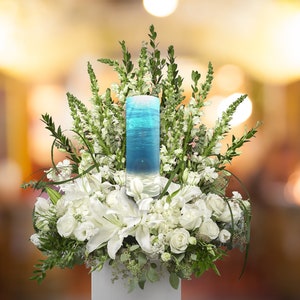 May include: A white flower arrangement with a blue glass cylinder filled with water and a blue and white design. The arrangement is in a white vase.
