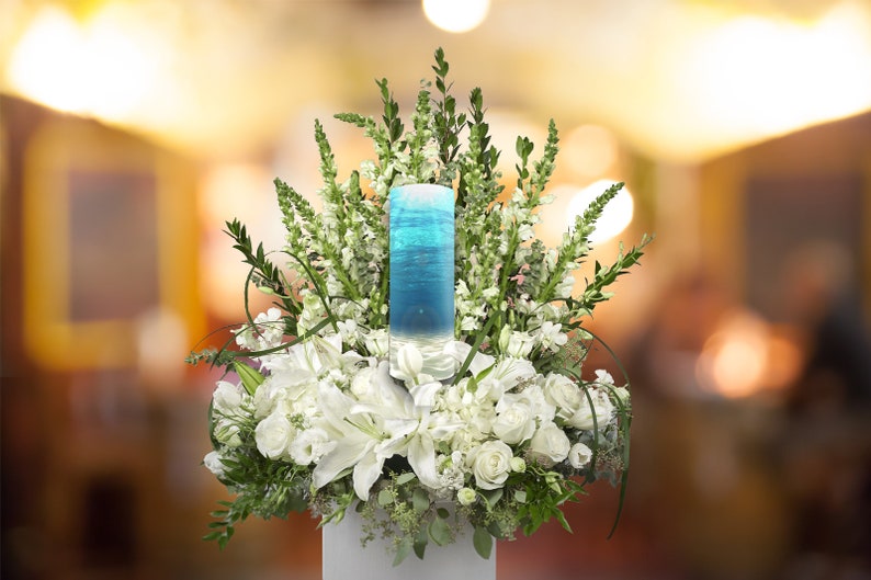 May include: A white flower arrangement with a blue glass cylinder filled with water and a blue and white design. The arrangement is in a white vase.