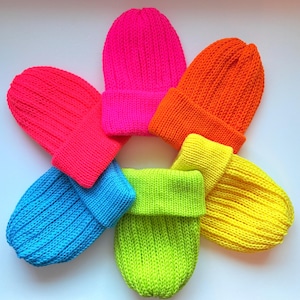 May include: A collection of six brightly colored knit beanies in a circular arrangement. The beanies are in shades of pink, orange, yellow, green, blue, and pink. Each beanie has a folded cuff and a ribbed knit texture.