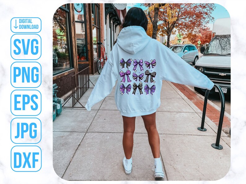 May include: A white hoodie with a design of purple, black, and gold bows on the back. The hoodie is being worn by a person standing on a sidewalk.