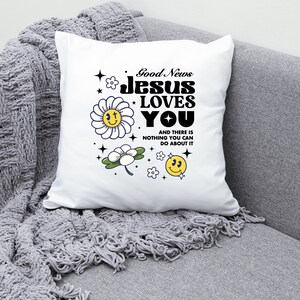 May include: White pillow with the text "Good News Jesus Loves You" in black bold letters. The text is surrounded by yellow smiley faces and white flowers with yellow centers.
