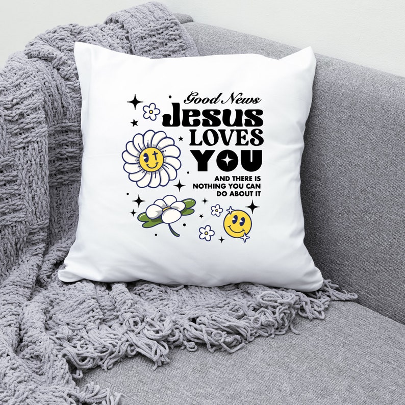 May include: White pillow with the text "Good News Jesus Loves You" in black bold letters. The text is surrounded by yellow smiley faces and white flowers with yellow centers.
