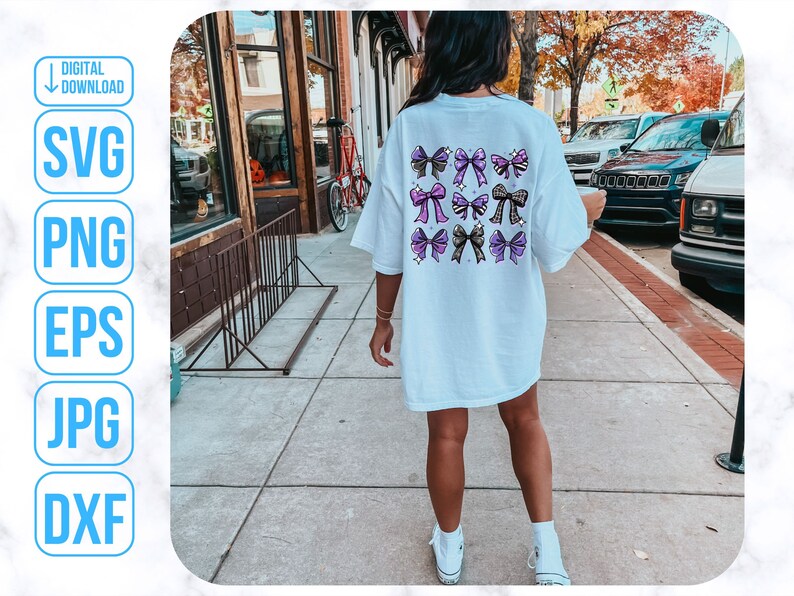 May include: A white t-shirt with a design of purple and black bows on the back. The shirt is being worn by a person walking down a sidewalk.