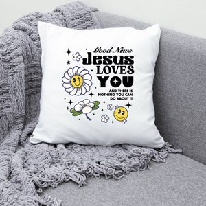 May include: White pillow with the text "Good News Jesus Loves You" in black bold letters. The text is surrounded by yellow smiley faces and white flowers with yellow centers.
