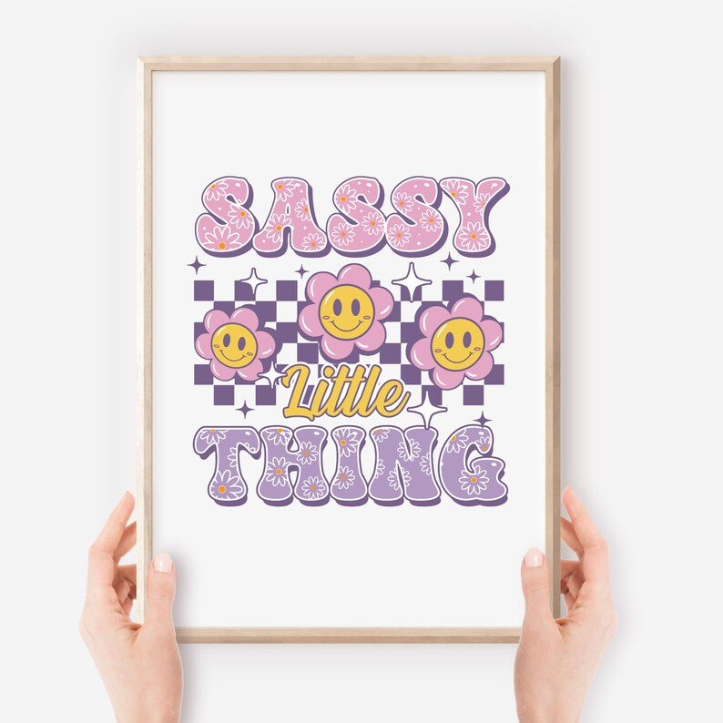 May include: A framed print with the words "SASSY LITTLE THING" in a retro font. The word "SASSY" is in pink with daisy accents, and "LITTLE THING" is in lavender. Smiley face flowers and a checkerboard pattern are also featured.
