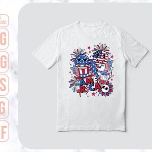 May include: White t-shirt with a cartoon design featuring two characters with American flag colors and the word "America" in red, white, and blue letters. The design also includes fireworks, stars, and a popsicle.
