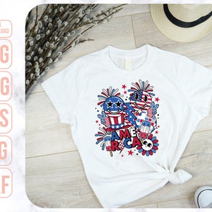 May include: White t-shirt with a red, white, and blue graphic design featuring cartoon characters, fireworks, and the word "America".