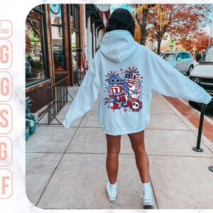May include: A light blue hoodie with a graphic design on the back. The design features a cartoon-style American flag, fireworks, and the word "America".