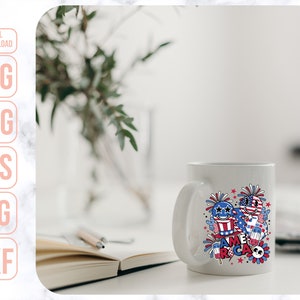 May include: White ceramic mug with a colorful design featuring fireworks, stars, and the word "America". The design is in red, white, and blue.
