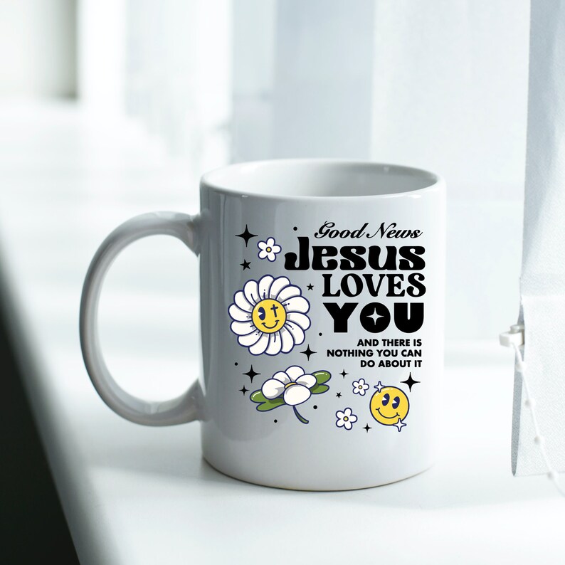 May include: White ceramic mug with a black and white graphic that says "Good News Jesus Loves You" and a daisy with a smiley face. There are other daisies and a smiley face on the mug.