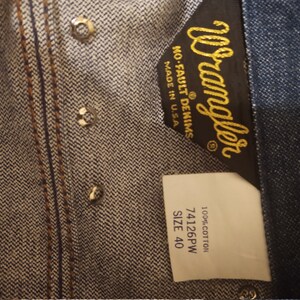 May include: A blue denim Wrangler label with the text "Wrangler No-Fault Denims Made in U.S.A." and a white label with the text "100% Cotton 74126PW SIZE 40".