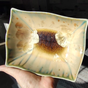 May include: A rectangular ceramic dish with a light brown glaze and a crackled finish. The dish has a light blue and green glaze around the edges. The dish is decorated with a brown and white design in the center.