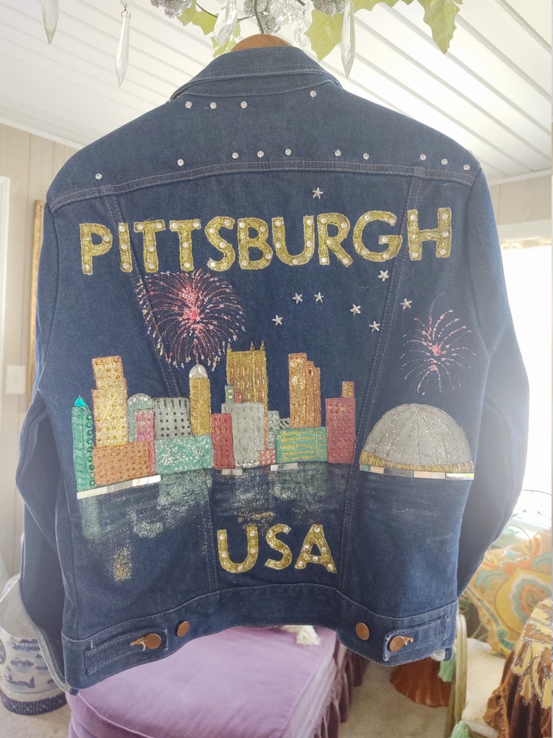 May include: A blue denim jacket with a gold glitter design of the Pittsburgh skyline and the words "PITTSBURGH USA".