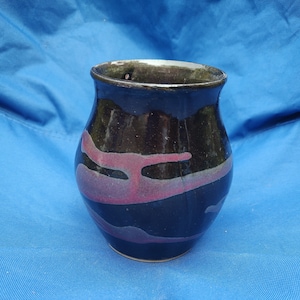 May include: A black ceramic vase with pink and purple abstract designs. The vase has a rounded body and a wide opening.