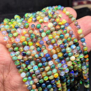 May include: Strands of colorful opal beads. The beads display a variety of colors, including blues, greens, yellows, and oranges. The beads are round and appear to be strung together, creating a necklace or bracelet.