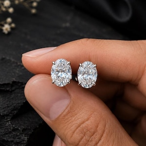 Può includere: Un paio di orecchini a lobo con pietre trasparenti dal taglio ovale sfaccettato, montate su metallo color argento lucido. Gli orecchini sono presentati insieme, mettendo in risalto la brillantezza e la forma ovale simmetrica delle pietre.